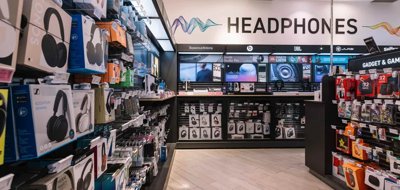Electronics store headphone section, displaying various branded headphones and accessories in colourful packaging on shelves.