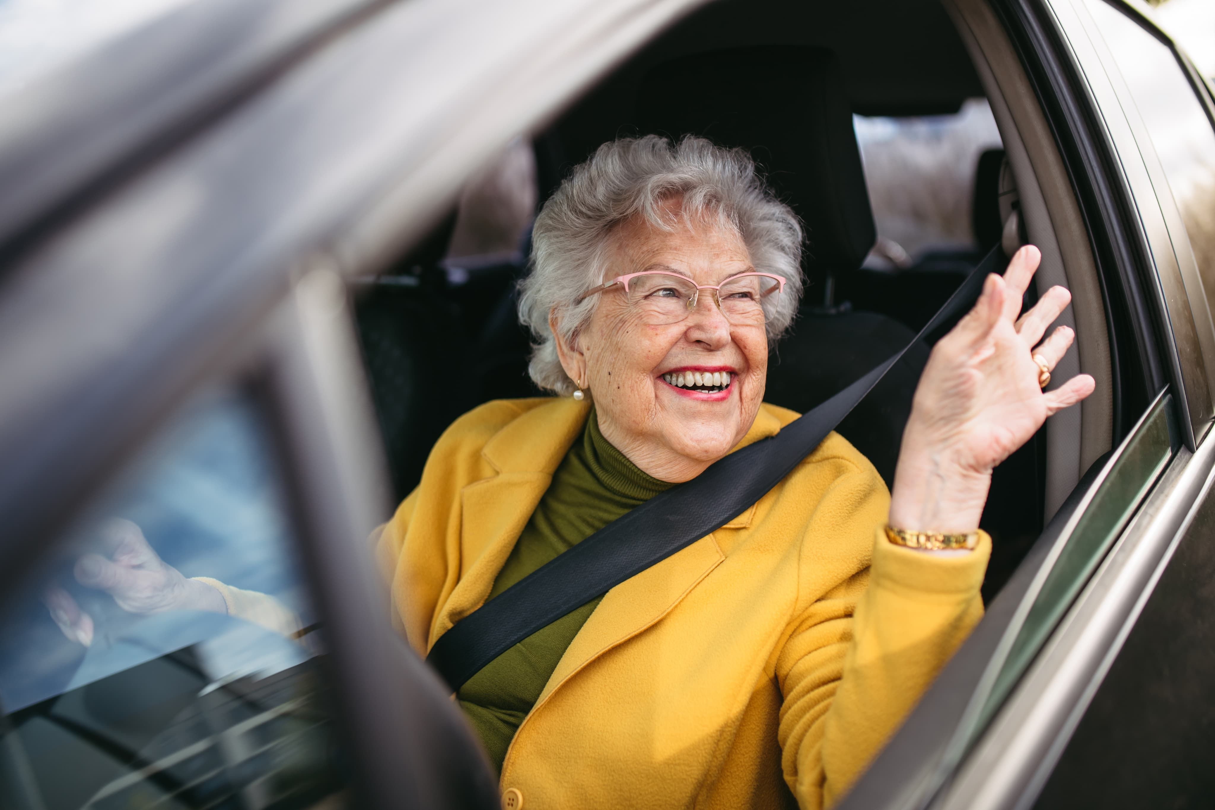 Elderly woman waving out of car window