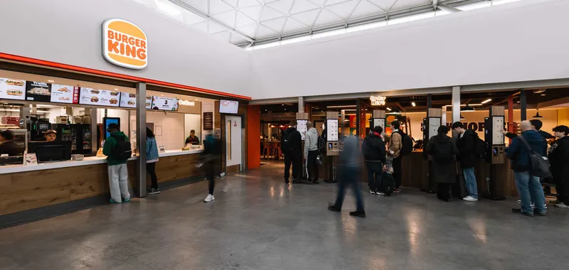 People ordering at a Burger King counter inside a modern, spacious food court.