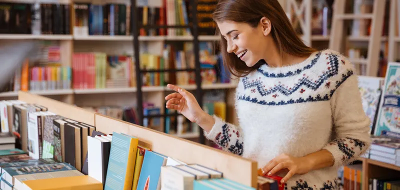 Woman laughing looking at books on shelf in shop