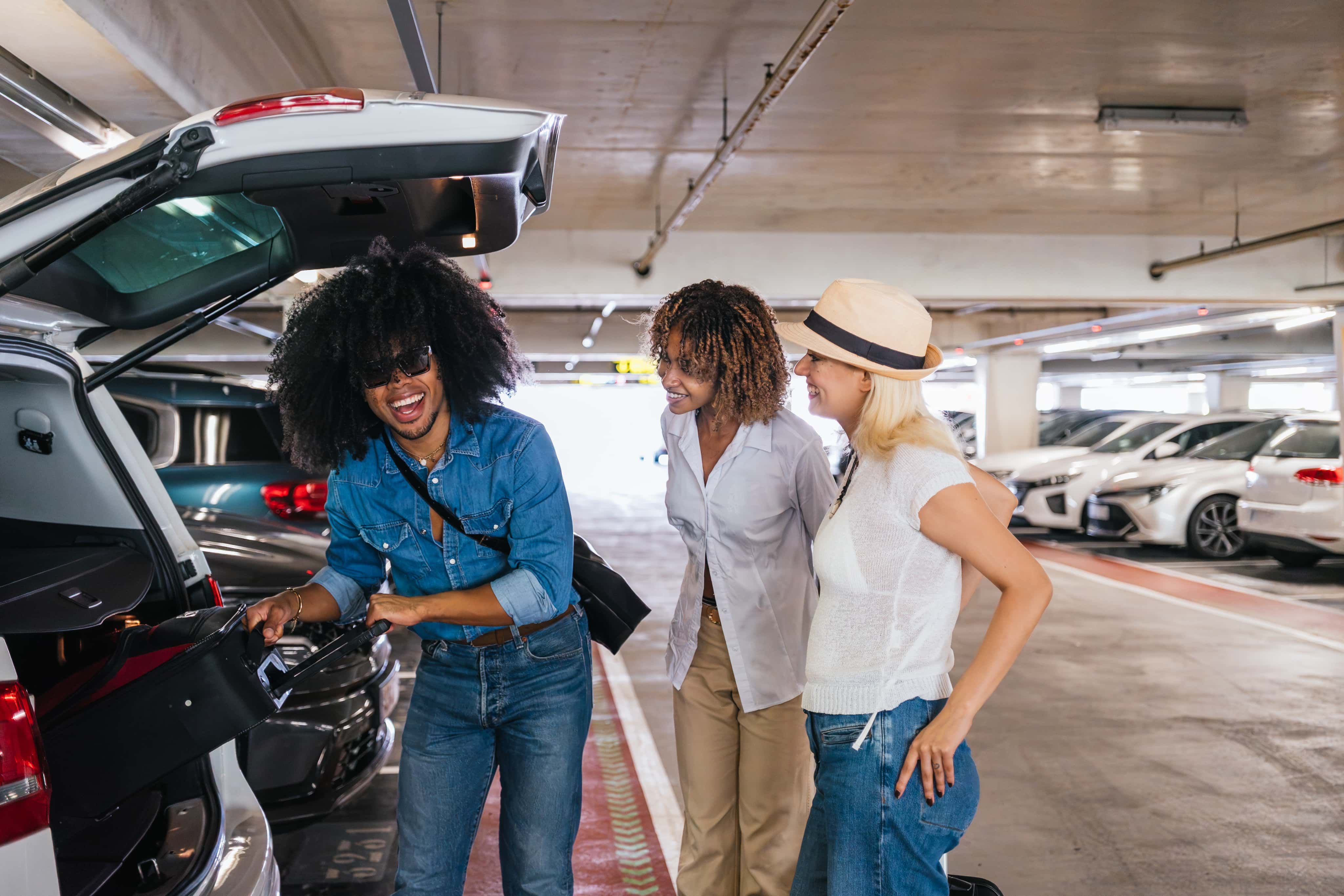 Three people getting luggage out of car boot