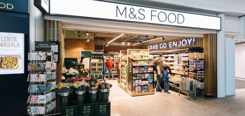 Entrance of M&S Food store with cards, flowers for sale outside; interior shows shelves stocked with groceries.