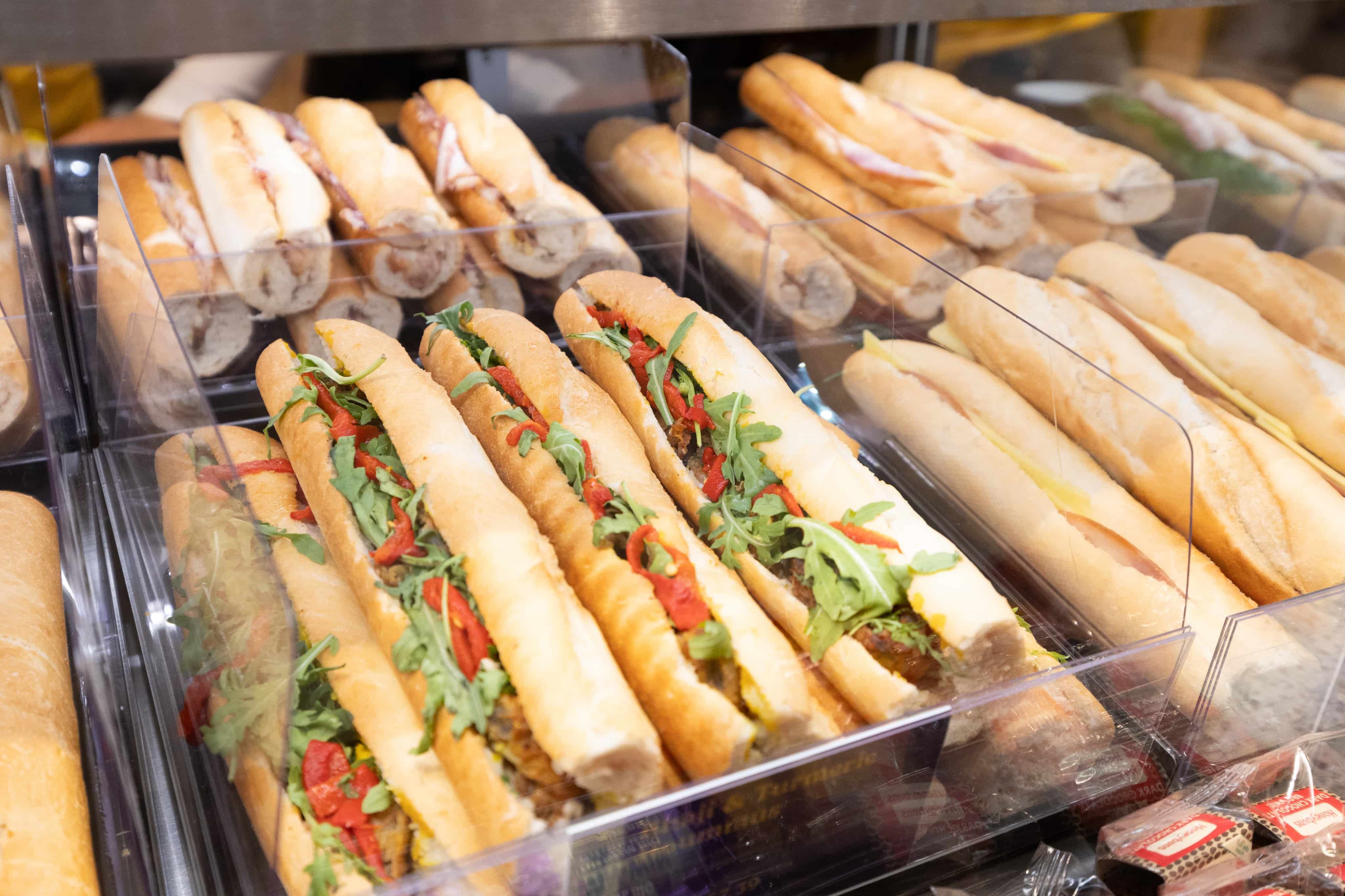 A display of various baguette sandwiches filled with lettuce, cheese, and sliced meats, arranged neatly in a transparent case.