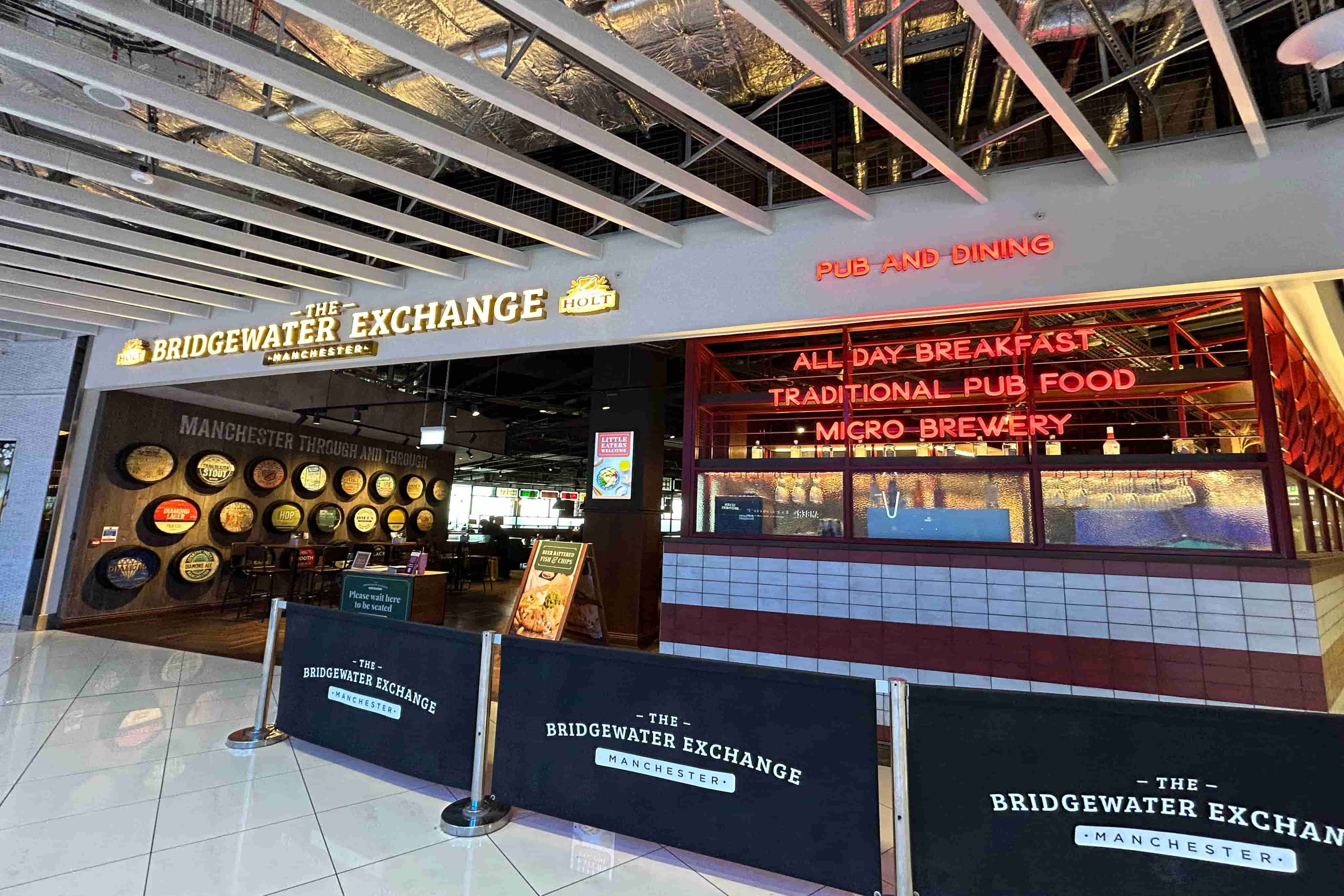 Entrance of The Bridgewater Exchange pub in Manchester with signs for breakfast, traditional pub food, and microbrewery beneath exposed ceilings.