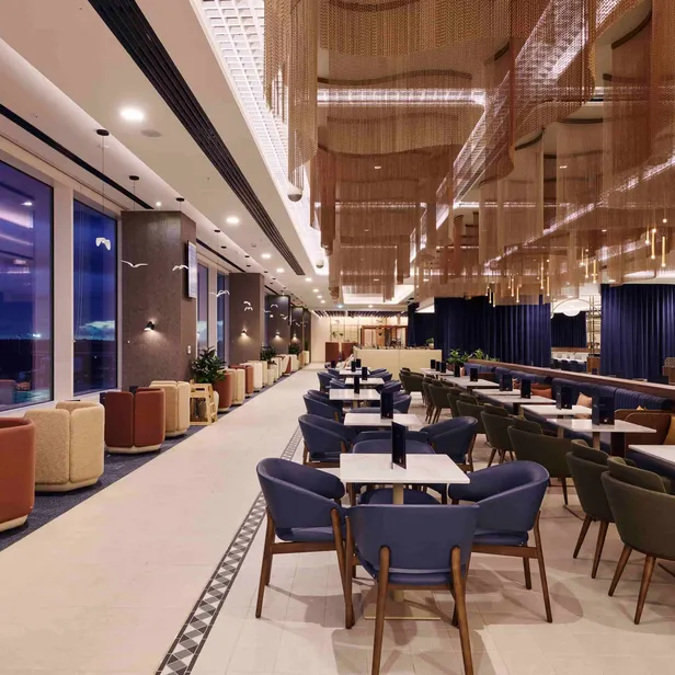 Spacious, modern restaurant interior with purple chairs, white tables, and large windows overlooking the view at dusk. Stylish lighting and decor.