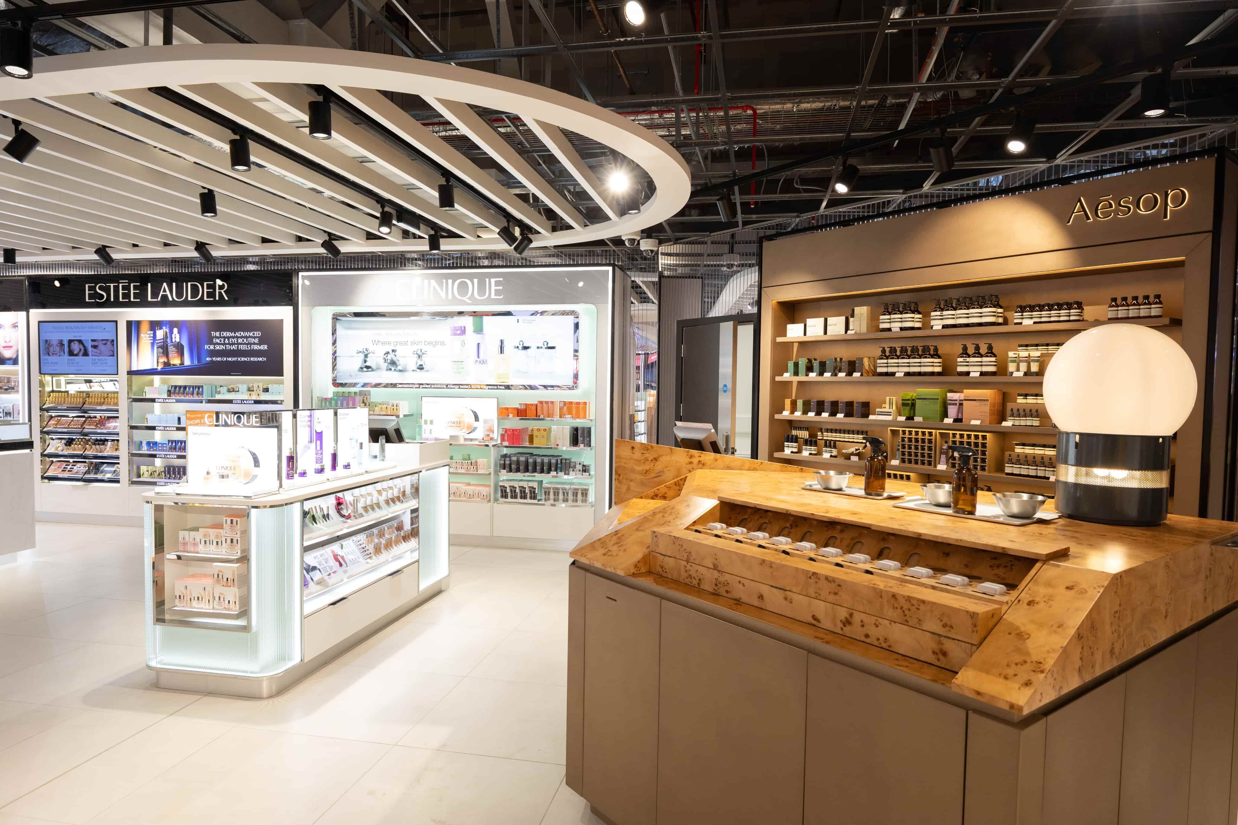 Modern cosmetics store interior with illuminated displays of Estée Lauder, Clinique, and Aesop products, featuring sleek white and wooden elements.