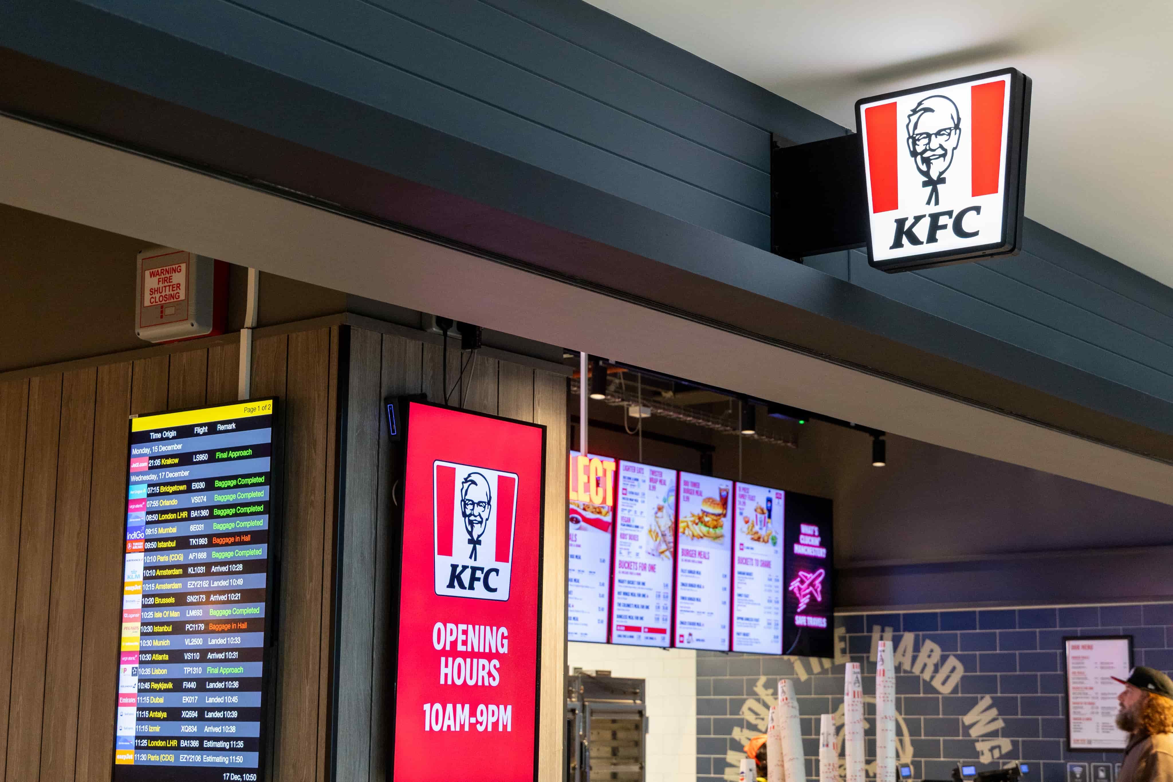 KFC restaurant with menu boards, a digital timetable, and an "Opening Hours 10AM-9PM" sign.