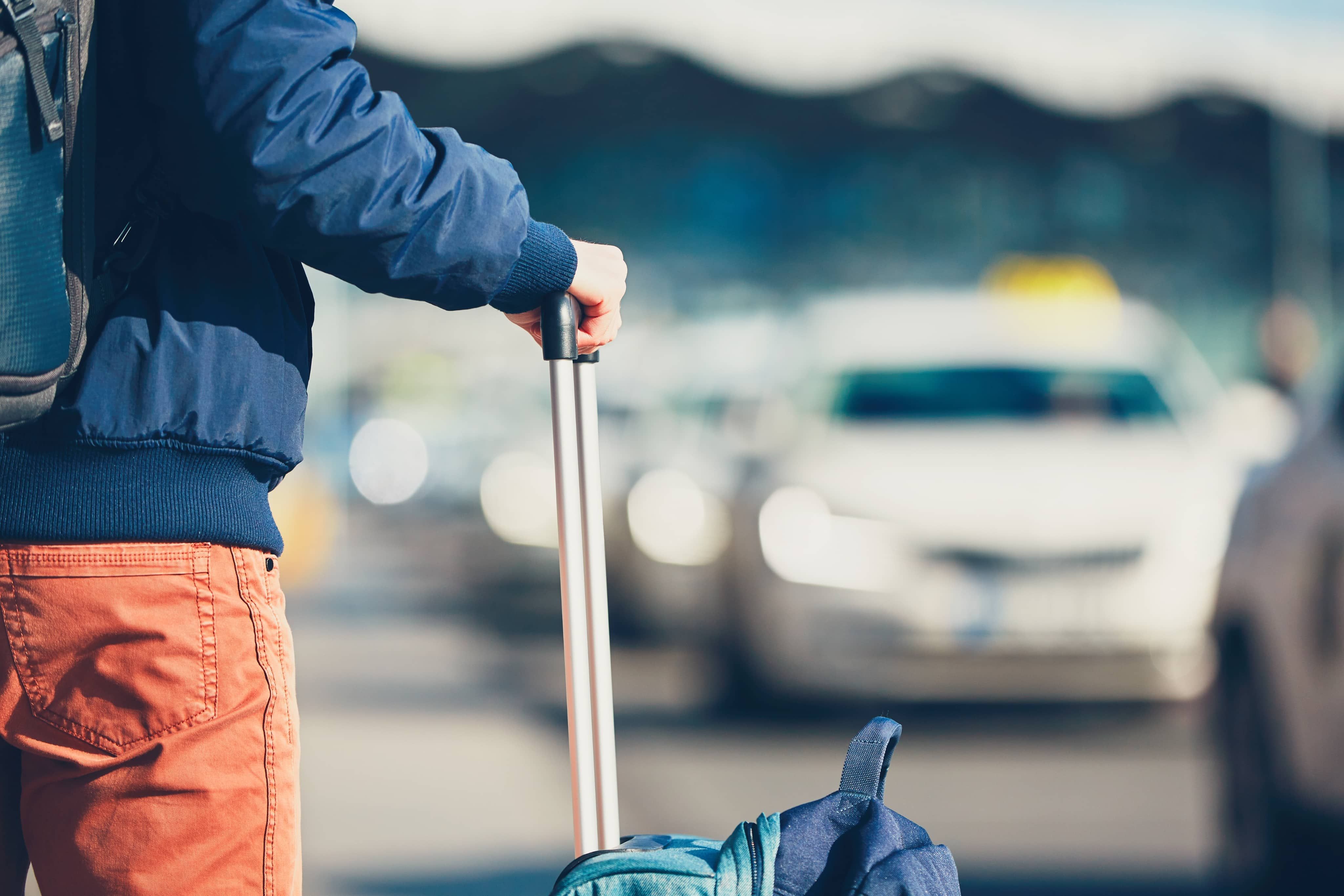 Close up of person holding suitcase handle with taxis in distance