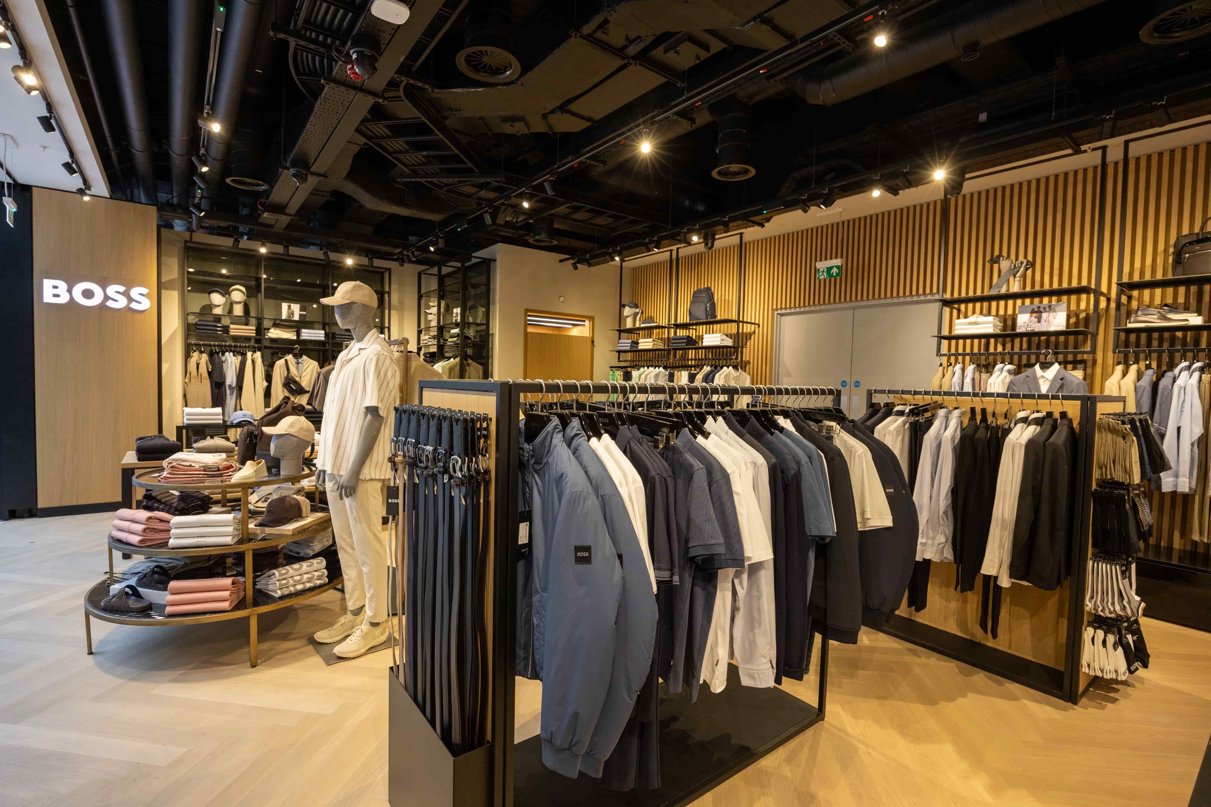 Clothing store interior with men's formal and casual wear on racks, a mannequin in neutral-colored attire, and neatly folded clothes on shelves.