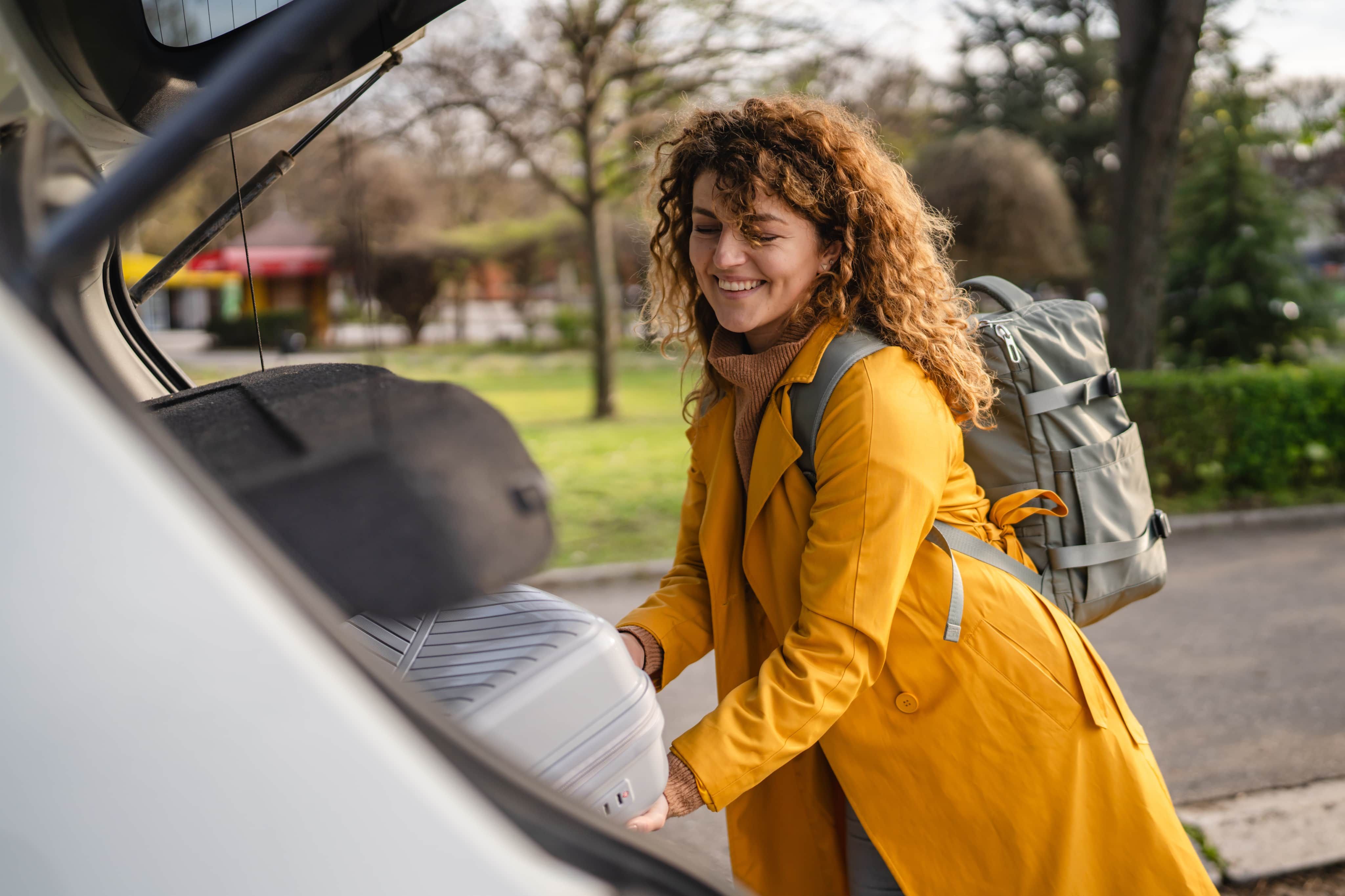 Woman putting luggage in car boot
