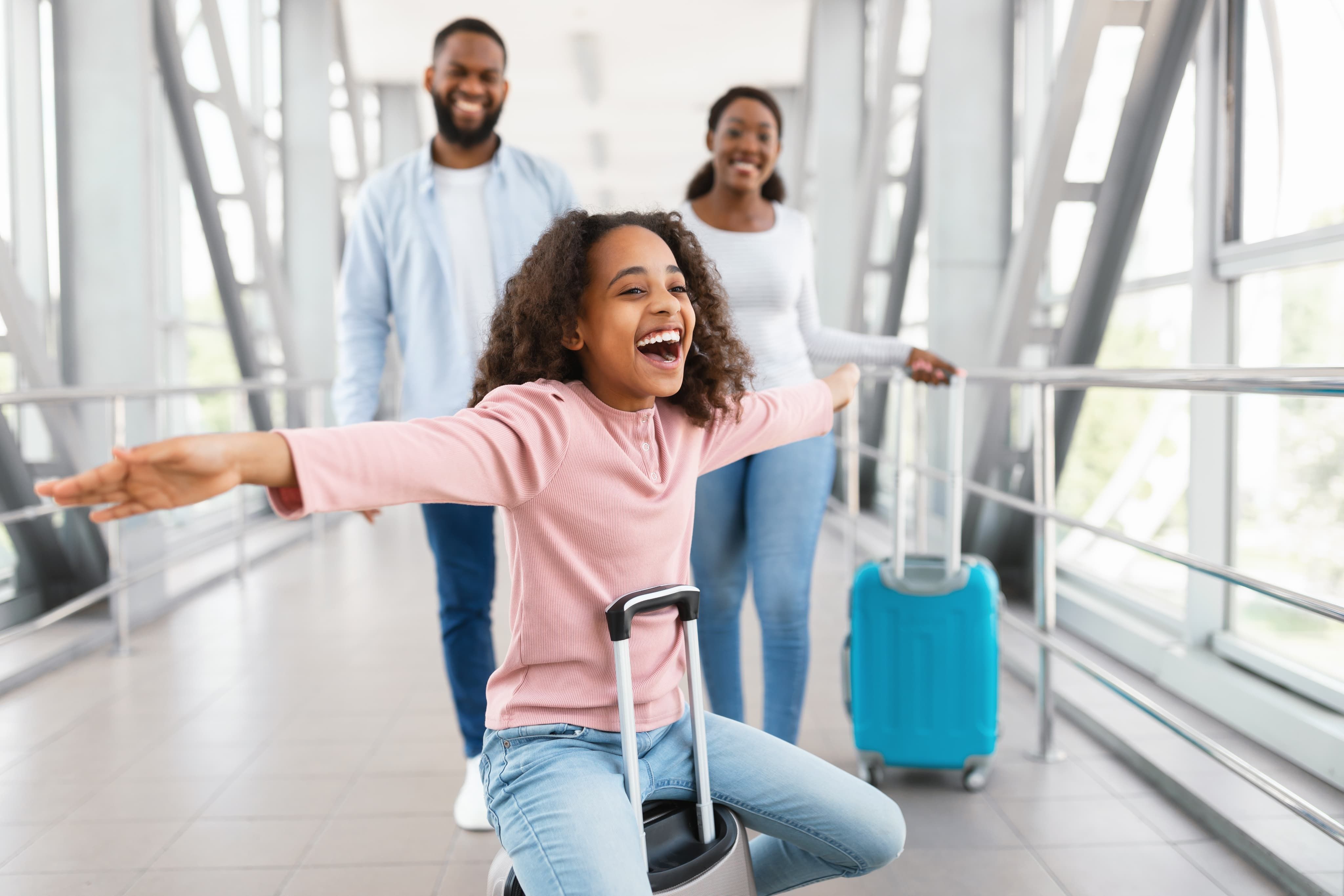 Girl sat on suitcase with parents behind