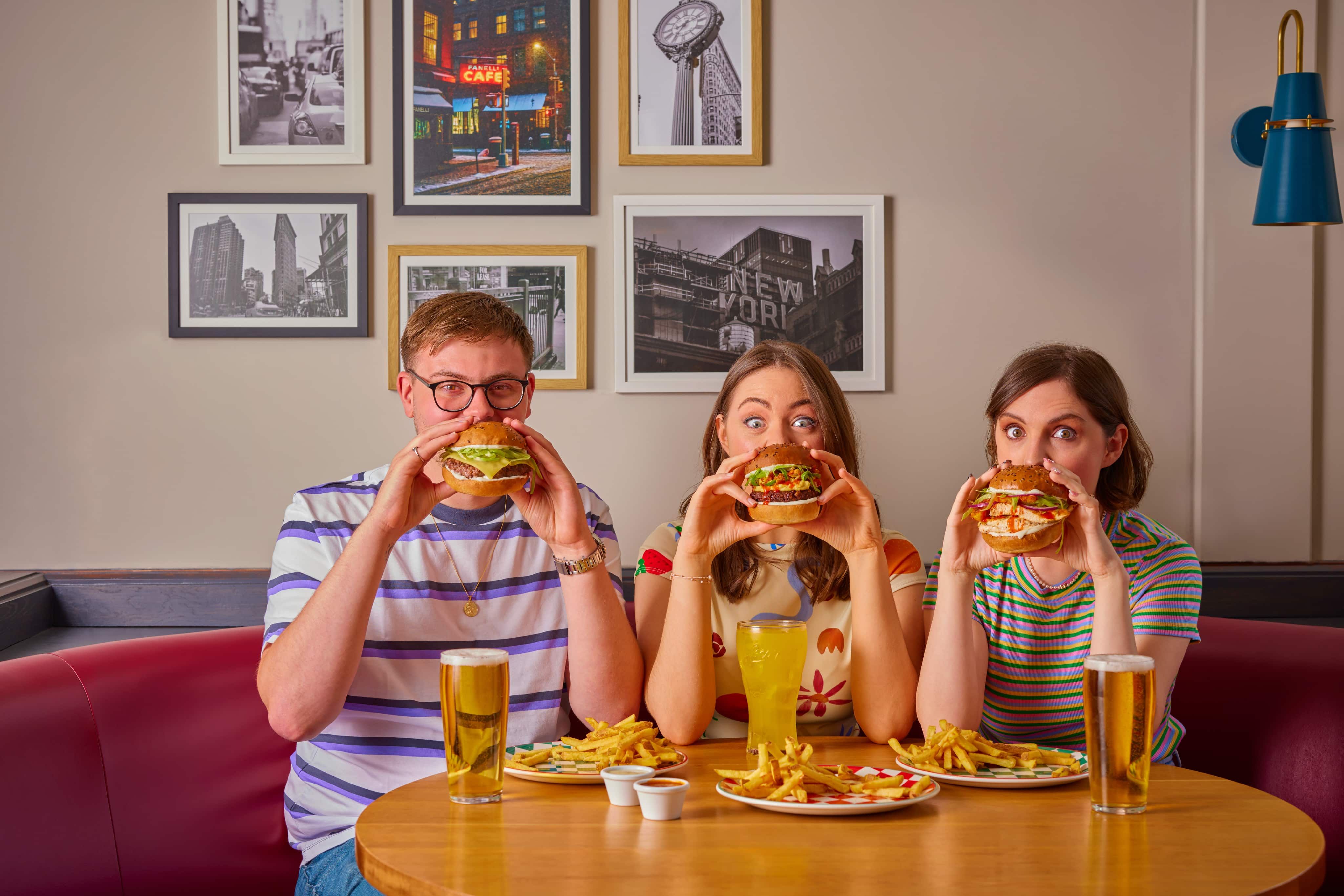 Two women and one man holding burgers in front of face