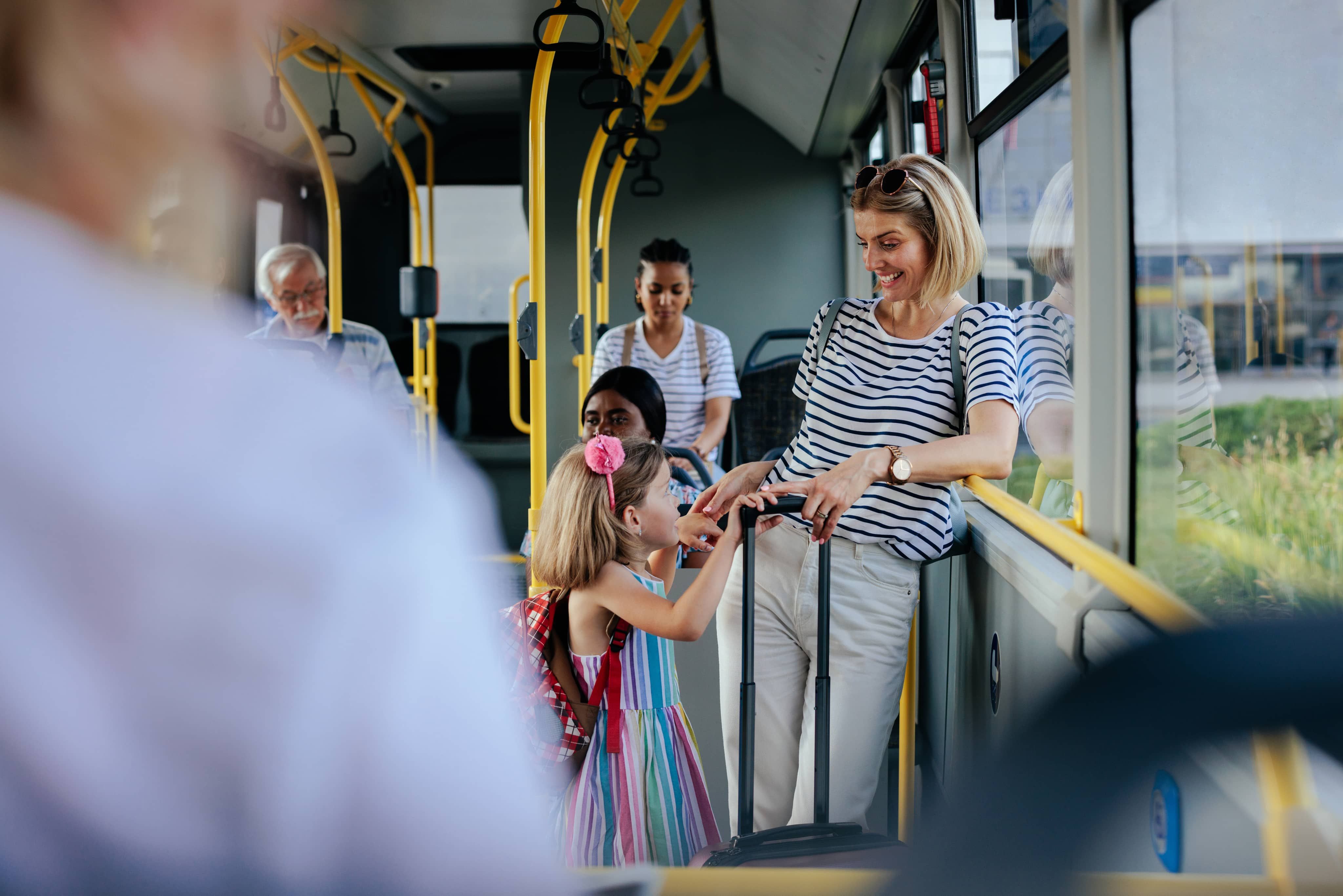 Woman and little girl smiling whilst standing on bus with luggage