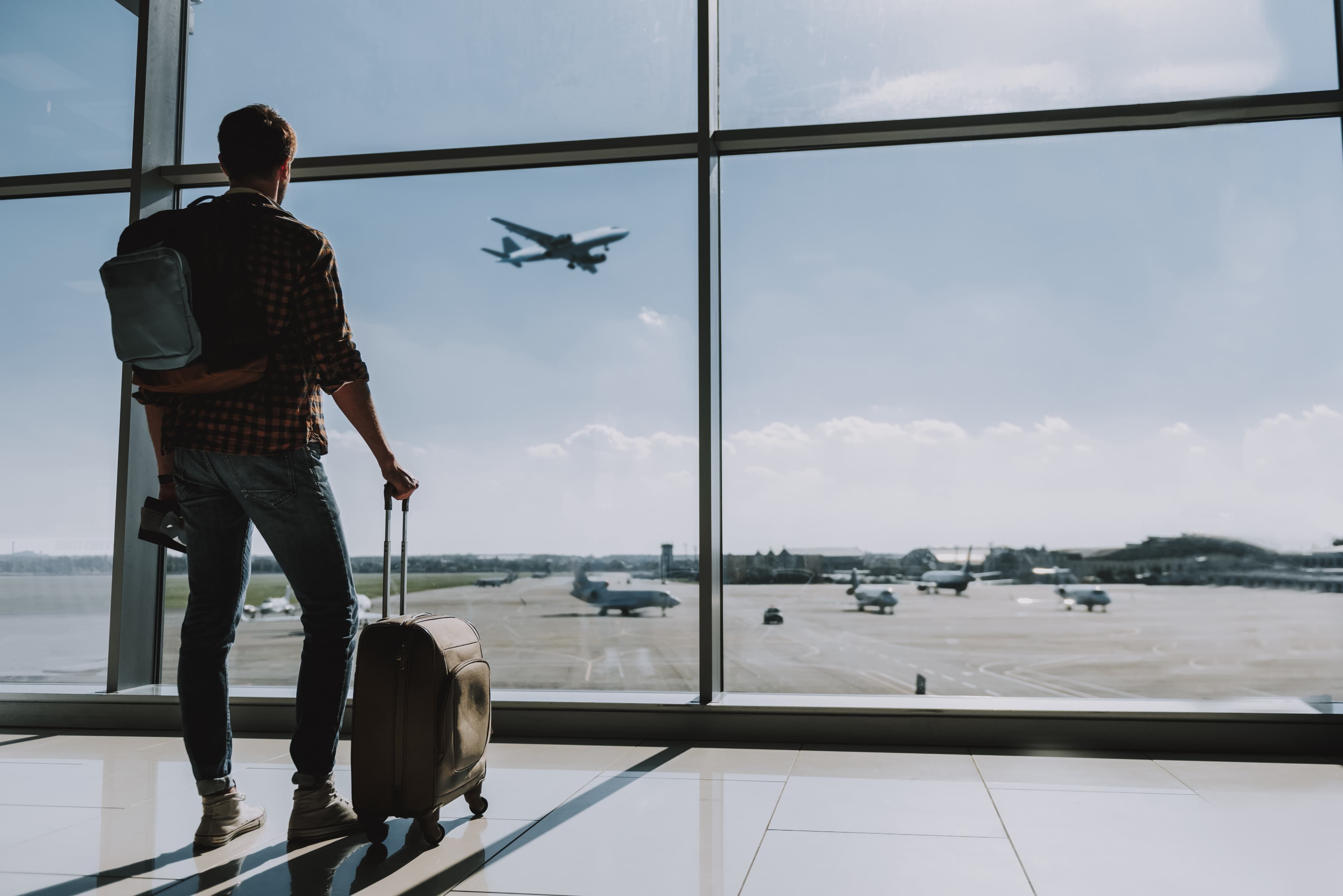 Man with suitcase watching plane out of window