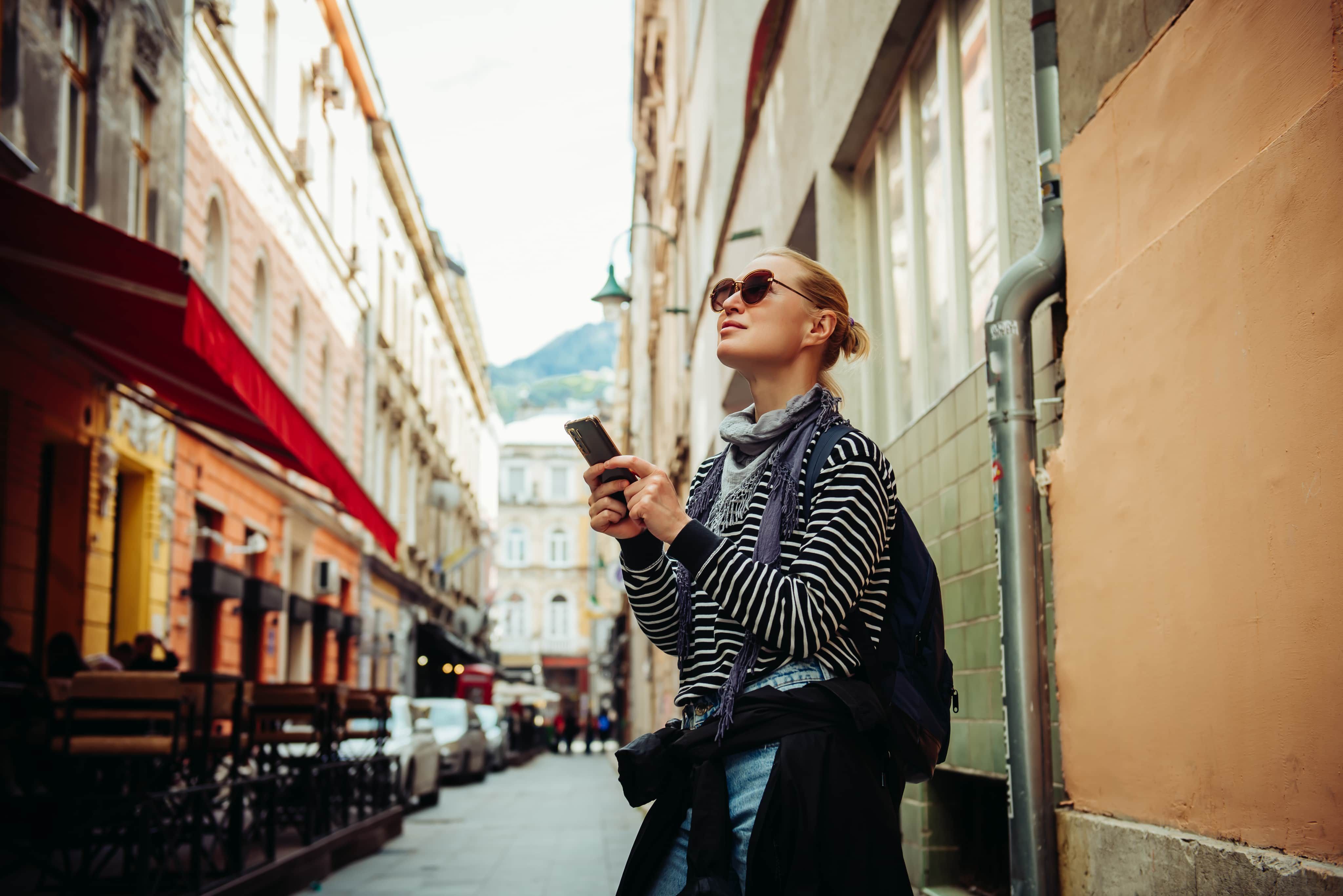 Woman holding phone looking up in street