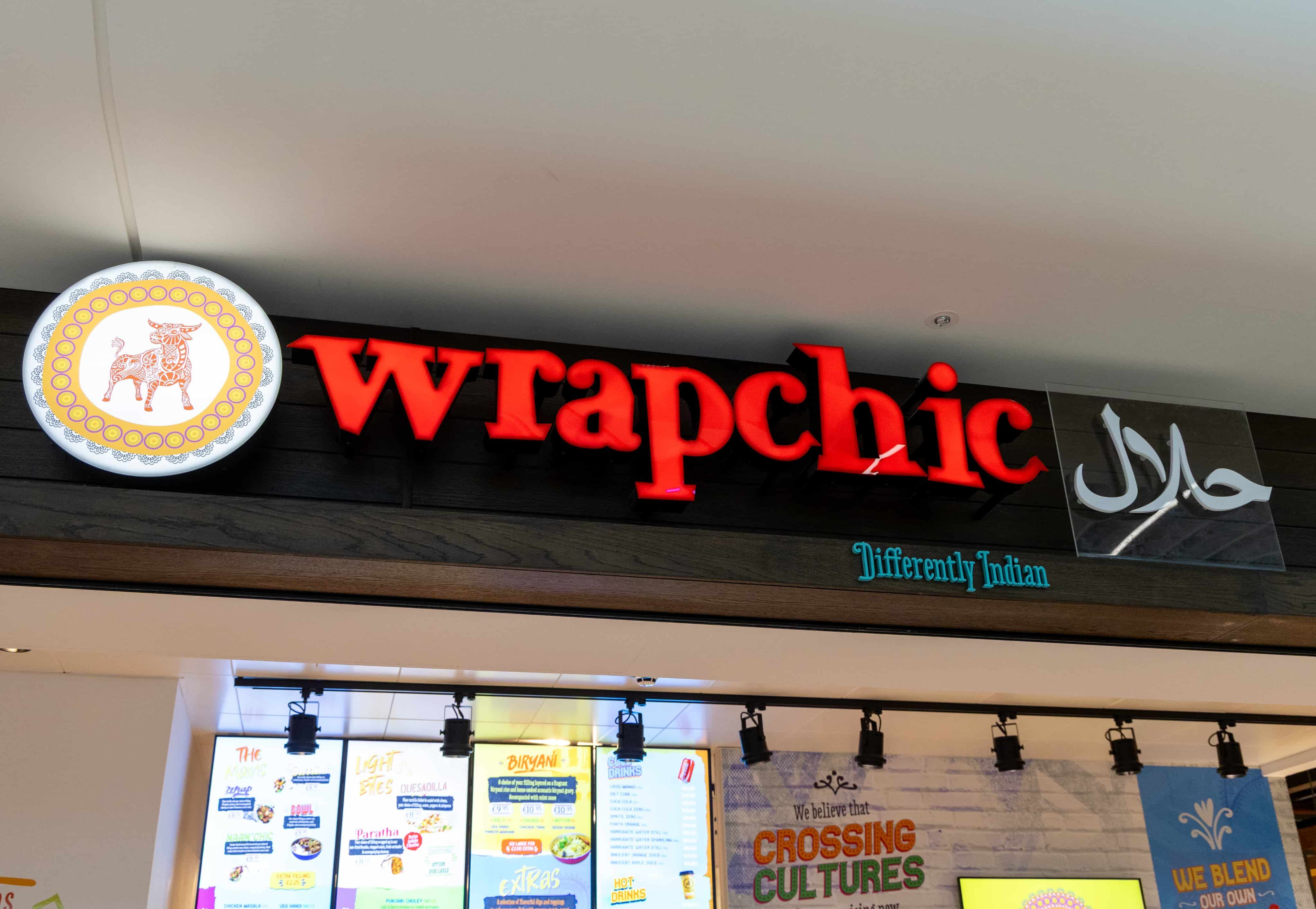 Storefront of "Wrapchic" with red lettering, displaying a "Halal" sign. Menu boards and "Differently Indian" tagline visible inside.