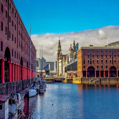 Scenic view of Albert Dock in Liverpool, with historic buildings, boats, and the Royal Liver Building under a blue sky.