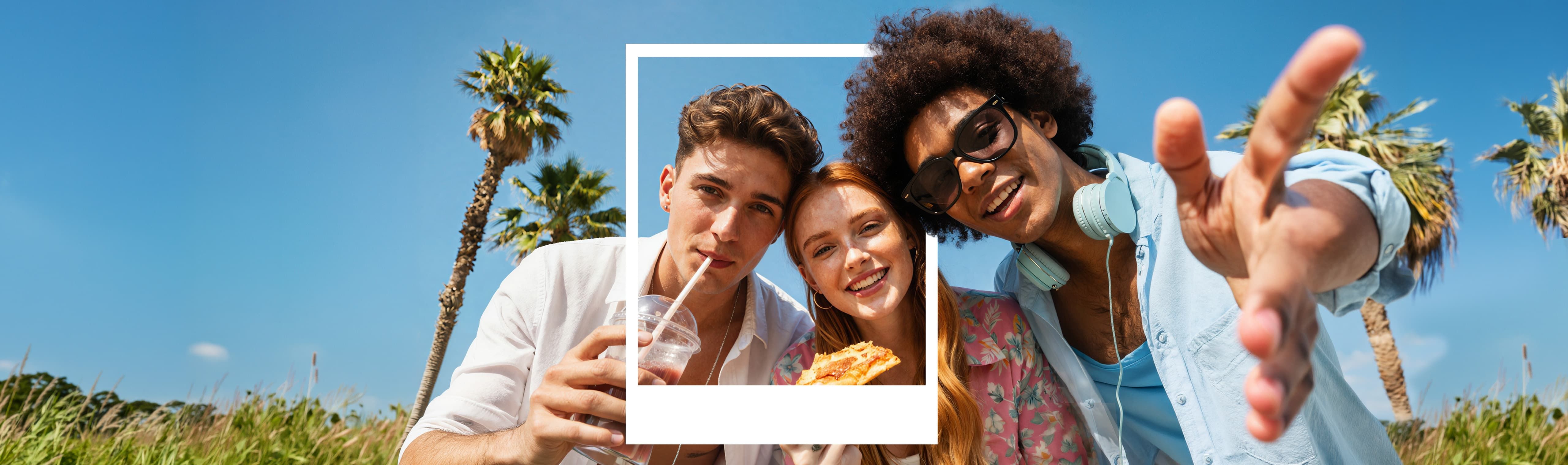 Three friends enjoying a sunny day outdoors, with palm trees in the background. One sipping a drink, another holding pizza, smiling at the camera.