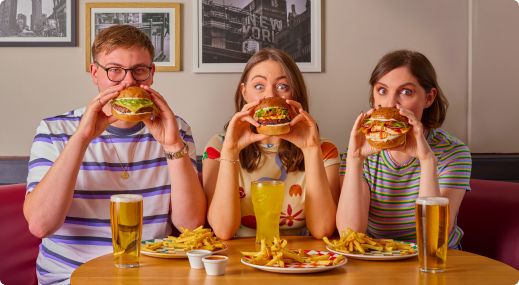 Two women and one man holding burgers in front of their face