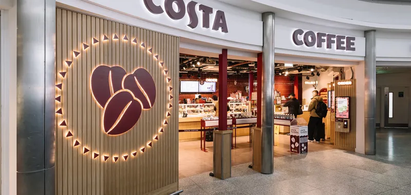 Costa Coffee shop entrance with illuminated coffee bean logo, modern décor, and customers ordering at the counter inside.