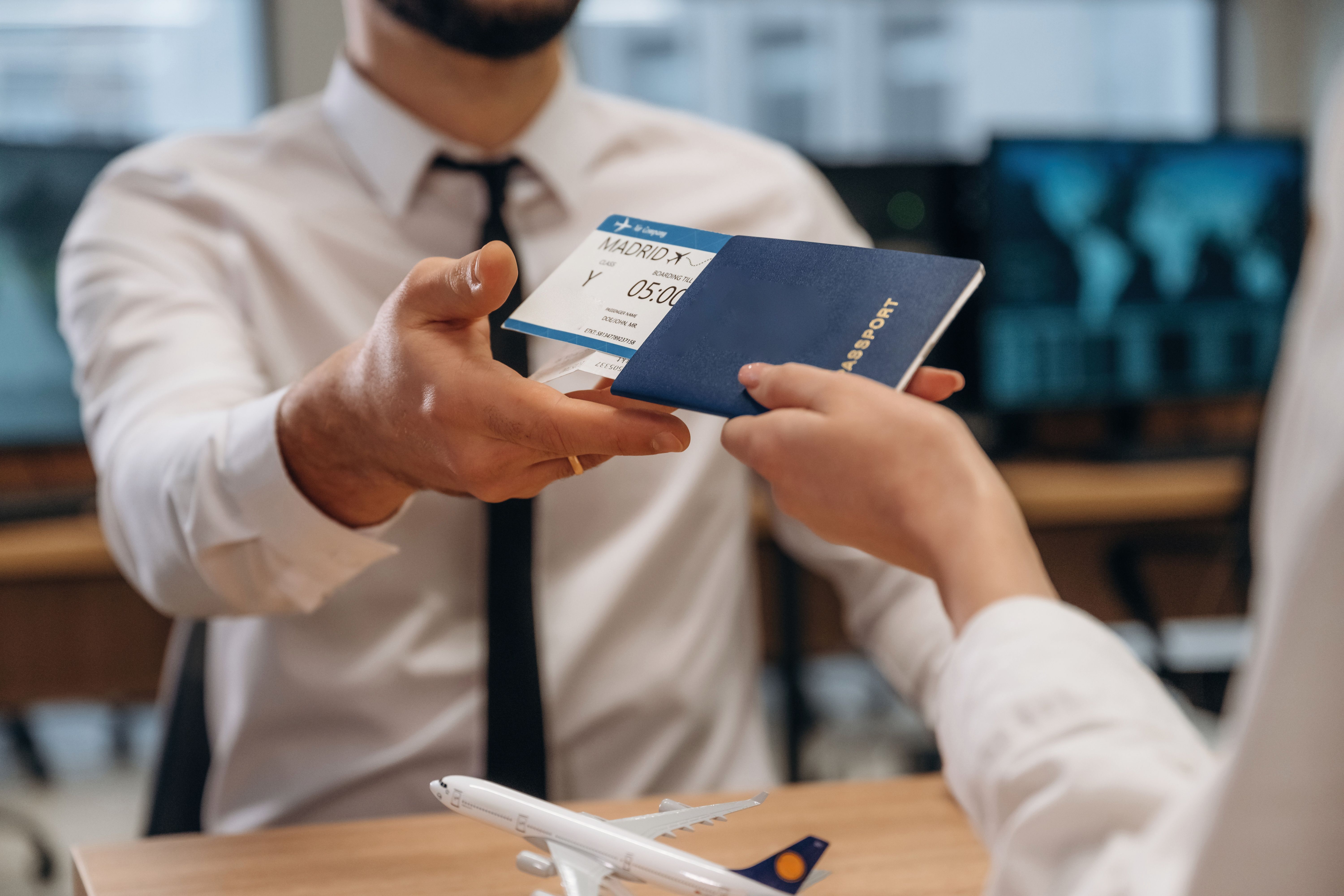 Man handing over a passport and boarding pass to another person in an office setting, with a model airplane on the desk.
