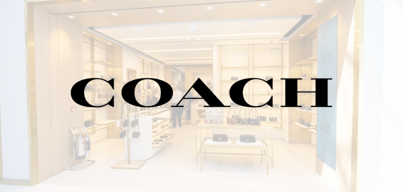 Storefront of a Coach retail shop displaying handbags and accessories, with the large "COACH" logo overlaying the image.