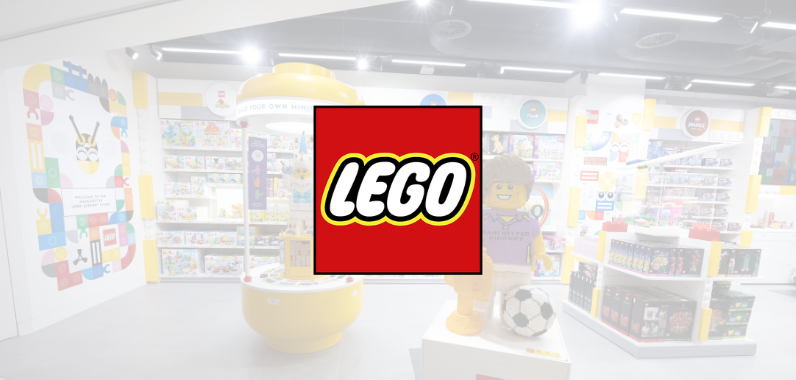LEGO logo centred over a bright, colourful toy store interior with shelves displaying various LEGO sets and products.