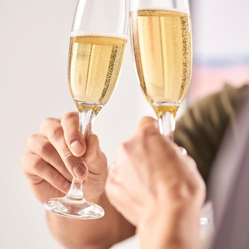 Two hands clinking champagne glasses filled with bubbly, golden liquid, set against a softly blurred background.