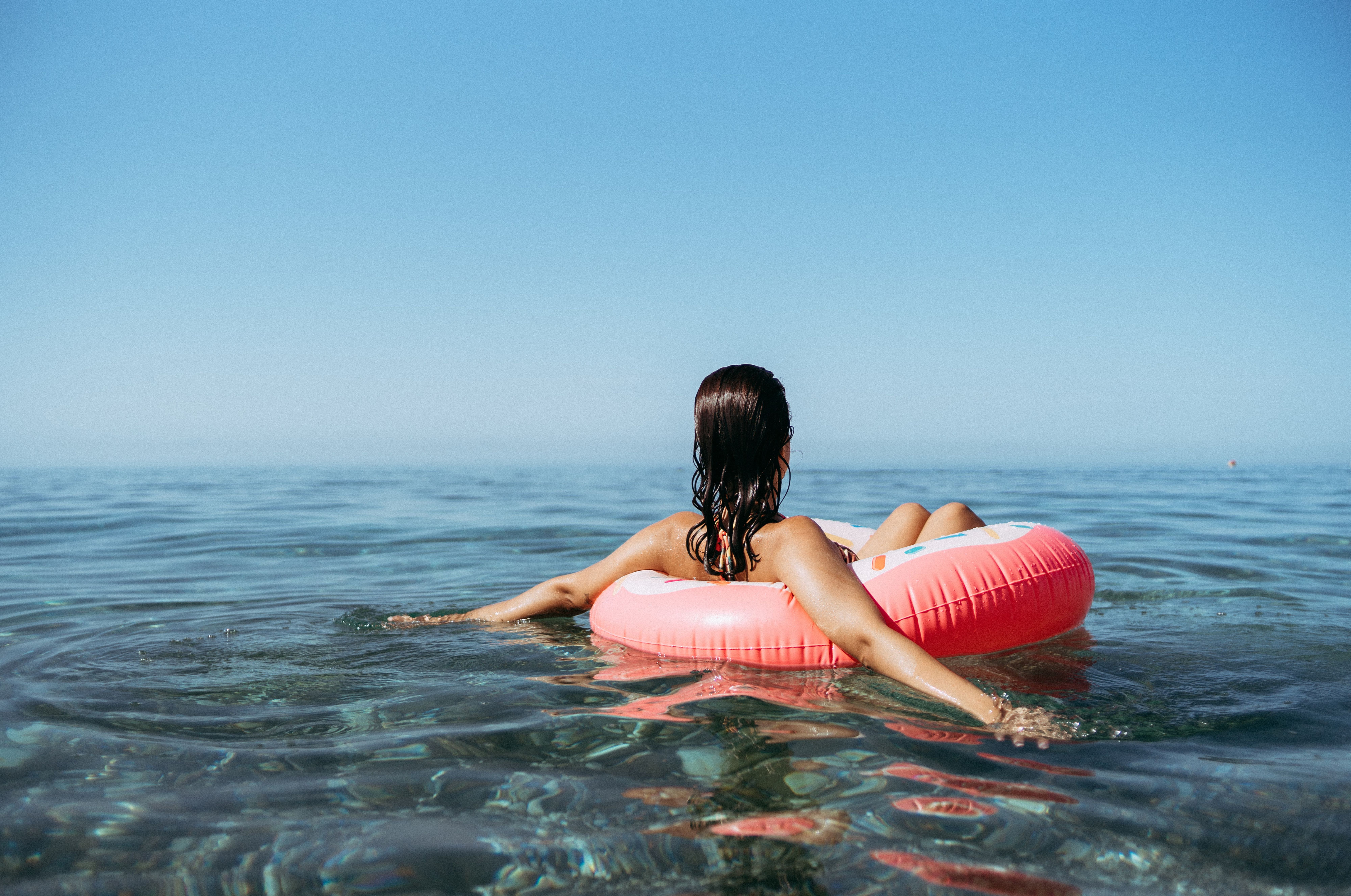 Person floating on a pink inflatable ring in the calm sea, under a clear blue sky.